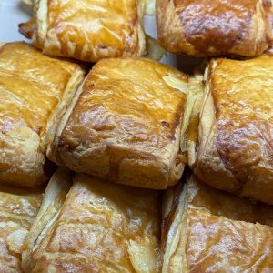 Pañuelos de hojaldre recién horneados, dorados y crujientes, rellenos de manzana y canela, dispuestos en una bandeja. Ideal para el desayuno o la merienda.