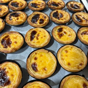 Tartas de crema pastelera recién horneadas, con una base crujiente y un acabado dorado, dispuestas en una bandeja de horno.