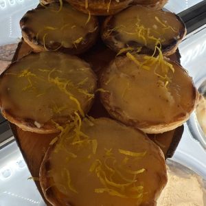 Tarta de limón con glaseado brillante y ralladura de limón, presentada en una bandeja de madera. Ideal para postres y ocasiones especiales.