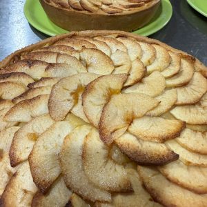Tarta de manzana recién horneada con una capa superior de rodajas de manzana doradas y caramelizadas, presentada en platos verdes.